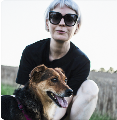 Regina Levenhagen steht mit einem schwarz braunen Tierschutzhund auf einer Wiese und blickt in die Kamera im Kontext positiven Hundetrainings